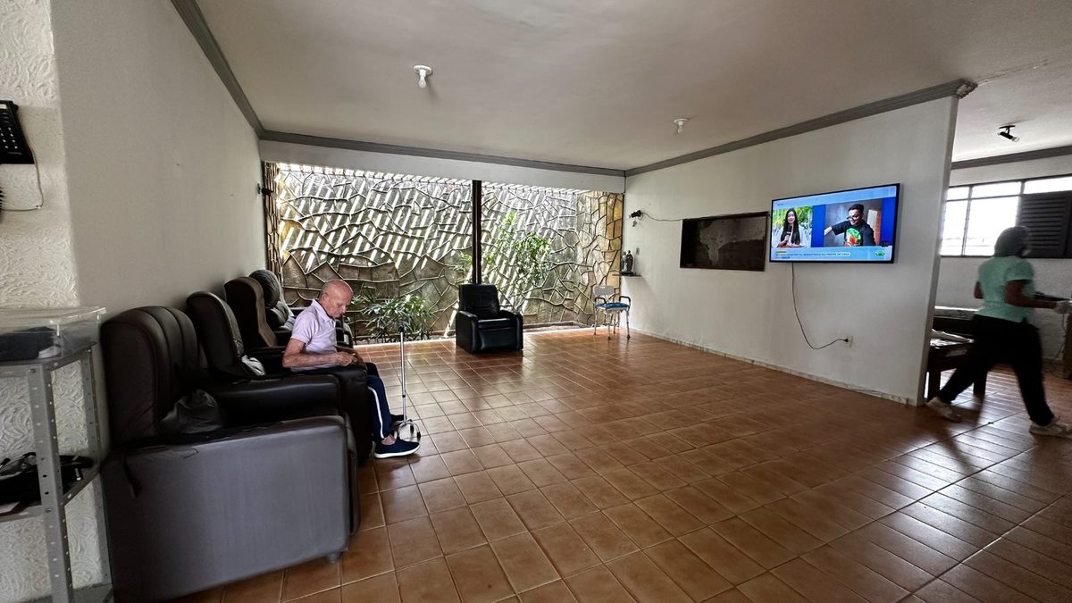 Sala de estar com poltronas reclináveis, televisão na parede e jardim interno com parede de pedras ao fundo